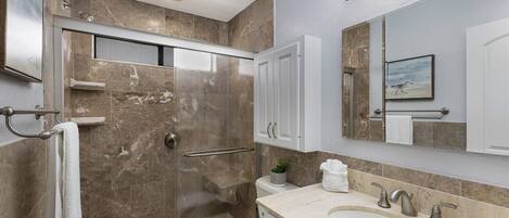 A modern bathroom with a glass shower enclosure, a toilet, a sink with a vanity, and a large mirror.