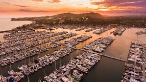 A marina with numerous boats docked, a hilly landscape in the background, and a sunset sky.