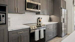 A modern kitchen with grey cabinets, a stainless steel microwave, a built-in oven, and a refrigerator. - NEW Rustic Villa – 2BD, 2BA Close to Beach and Everything! (Santa Barbara)