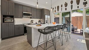 A modern kitchen with dark cabinets, stainless steel appliances, and a large island with bar stools. - NEW Rustic Villa – 2BD, 2BA Close to Beach and Everything! (Santa Barbara)