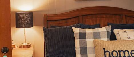 A bedroom with a wooden headboard, a bed with dark blue bedding, a checkered pillow, and a framed painting on the wall.