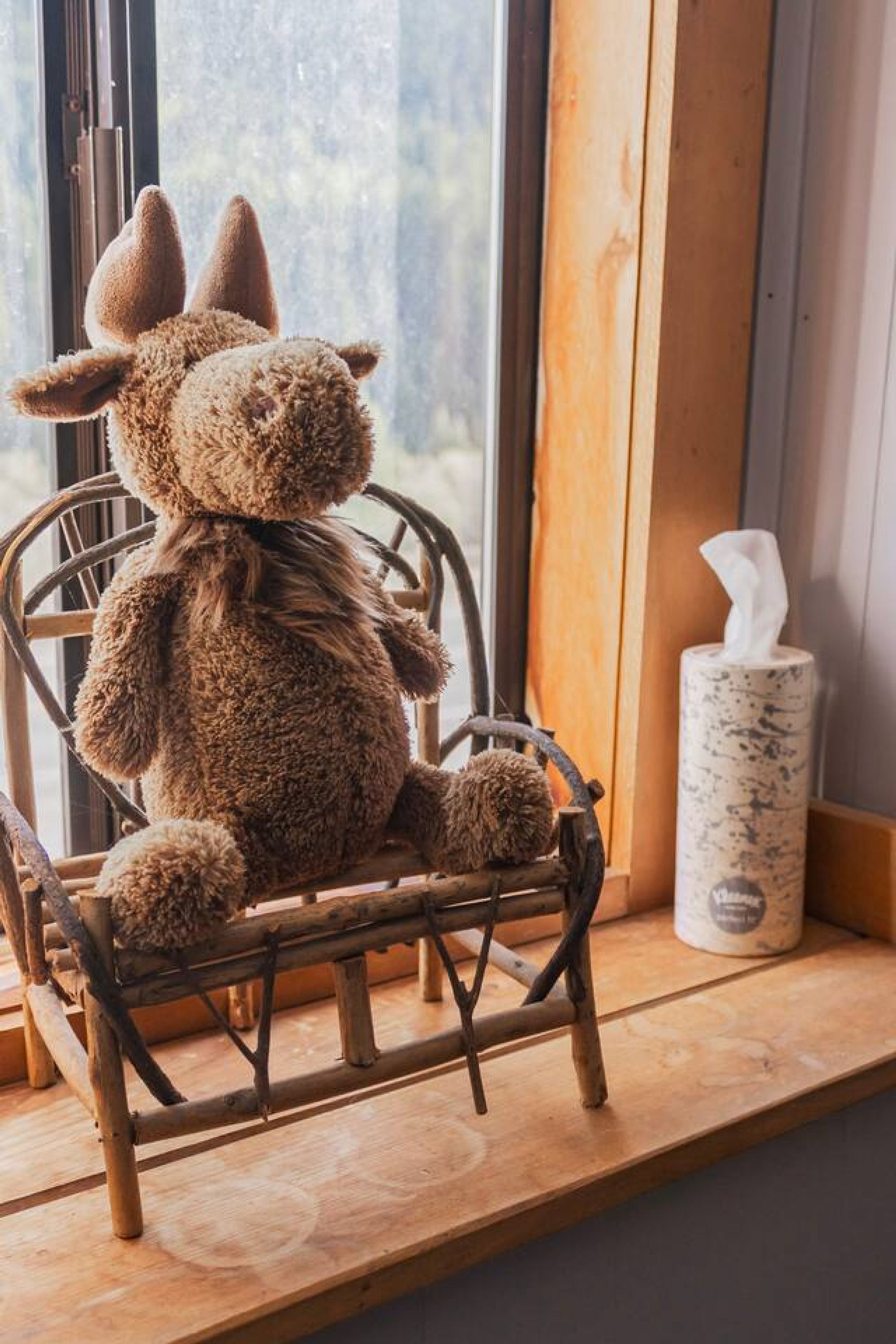 A plush toy rabbit sitting on a wicker chair by a window.