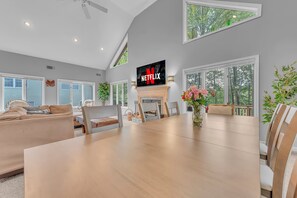 Ein modernes Wohnzimmer mit Kamin, Esstisch und einem darüber montierten Fernseher.