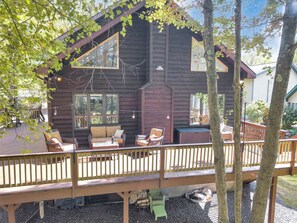Eine Holzhütte mit einer Terrasse, Sitzgelegenheiten im Freien und einem großen Fenster.