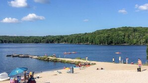 A lakeside beach with a dock, kayaks, and beach chairs. - Large Family Friendly House on the Fairway Hideout (Lake Ariel)