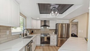 A modern kitchen with white cabinetry, stainless steel appliances, and a wooden ceiling. - Family Friendly Retreat near Clearwater Beach. (Safety Harbor)