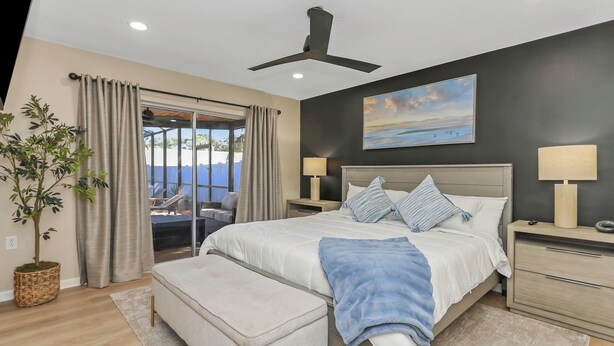 A modern bedroom with a large bed, bedside tables, a ceiling fan, and a view through a glass door. - Family Friendly Retreat near Clearwater Beach. (Safety Harbor)