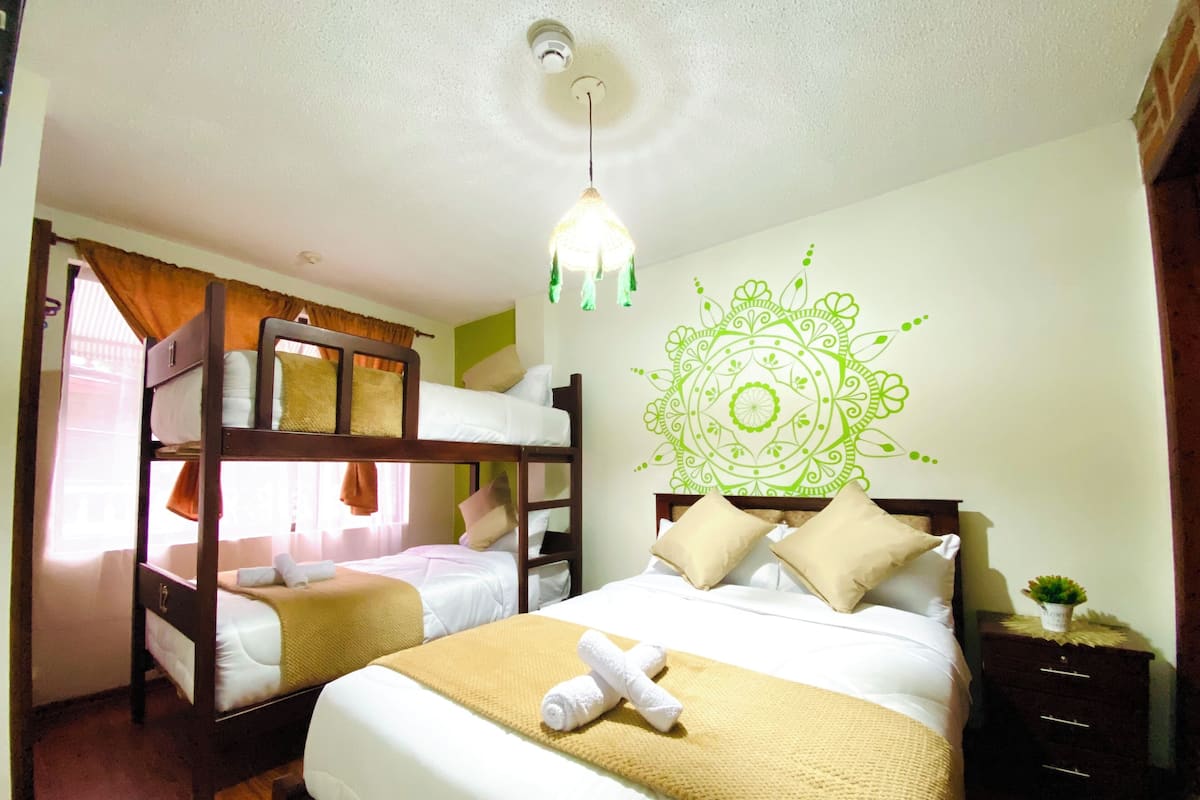Habitación de hotel con literas, una cama con decoración en la pared, una mesita de noche y una lámpara colgante.