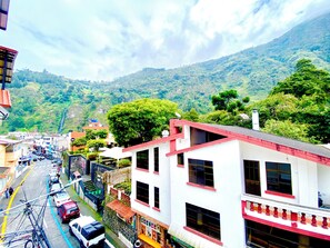 Une vue de rue avec des immeubles, des voitures garées et une chaîne de montagnes en arrière-plan.