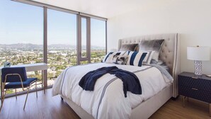 A bedroom with a large bed, a desk, and a chair, with a city view through large windows. - Visit LA in Ultra Luxury with Breathtaking Views (Beverly Hills)