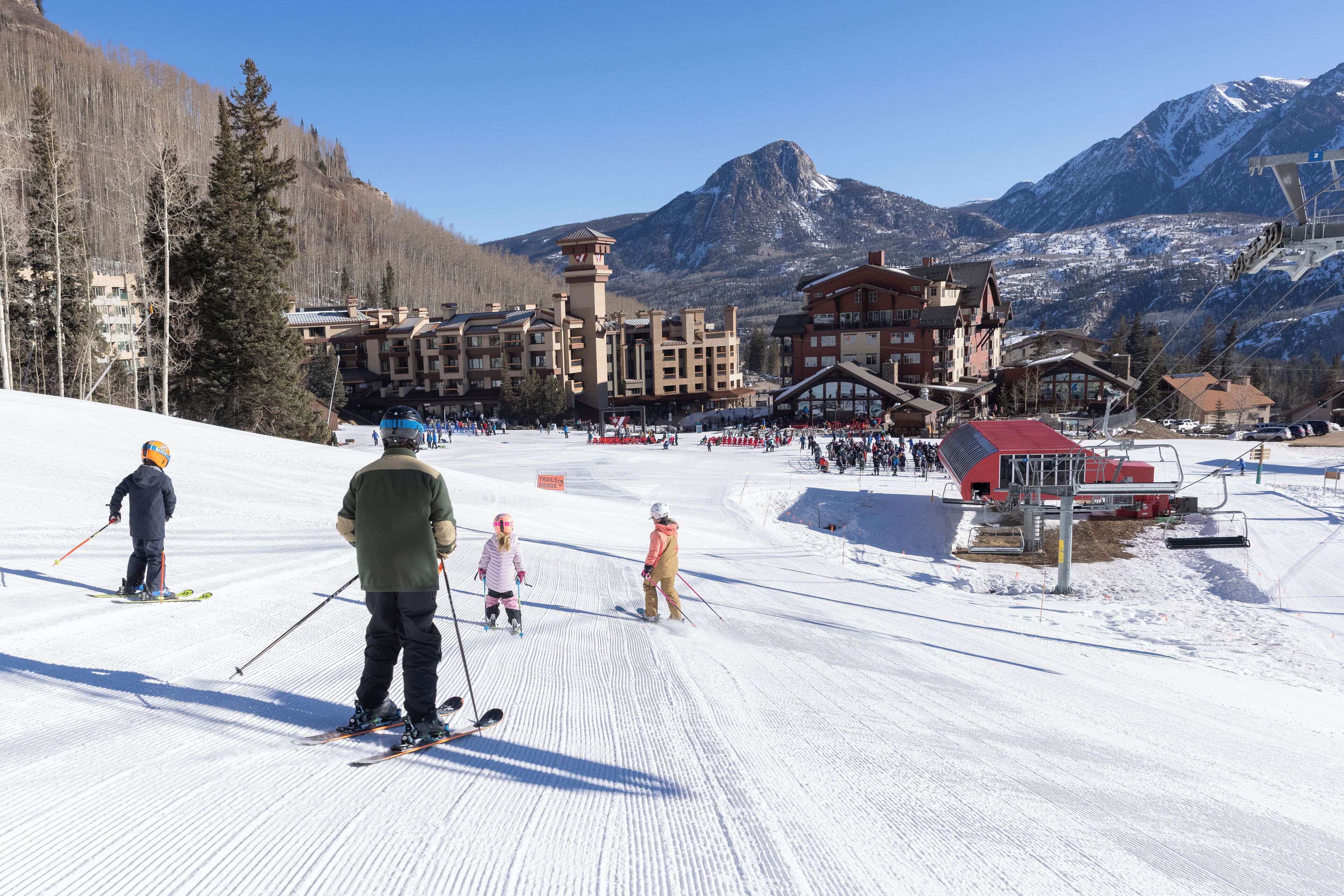 A ski resort with buildings, a ski lift, and a snowy mountain backdrop.