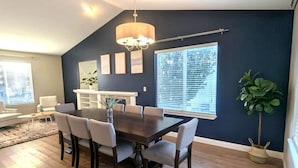 A dining area with a dark blue accent wall, a chandelier, and a large window with blinds.