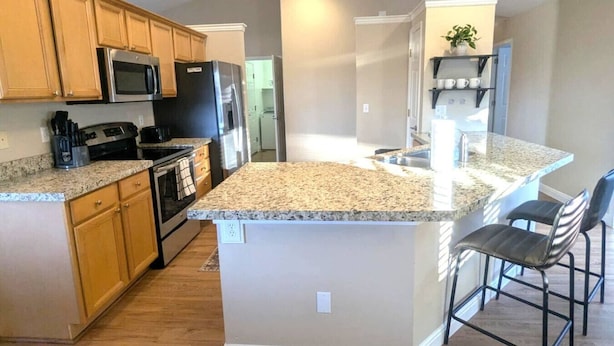 A modern kitchen with granite countertops, wooden cabinets, stainless steel appliances, and a central island with bar stools.