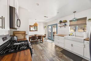 A kitchen with white cabinets, a wooden countertop, a gas stove, and a dining area with chairs.