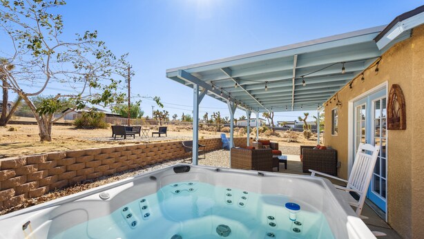 A hot tub with a covered patio area, a brick wall, and outdoor furniture. - Starlight Ranch with Hot Tub, Fire Pit & BBQ! (Joshua Tree)