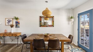 A dining area with a wooden table, four chairs, a hanging woven light fixture, and a colorful mirror on the wall. - Starlight Ranch with Hot tub, Fire pit & BBQ! (Joshua Tree)