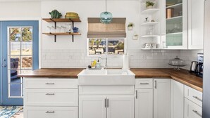 A kitchen with white cabinets, a wooden countertop, a window with a view, and a hanging light fixture. - Starlight Ranch with Hot tub, Fire pit & BBQ! (Joshua Tree)