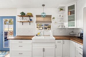 A kitchen with white cabinets, a wooden countertop, a window with a view, and a hanging light fixture.