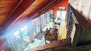 Un intérieur en bois aux plafonds hauts, comprenant un coin repas, une cuisine et de grandes fenêtres.
