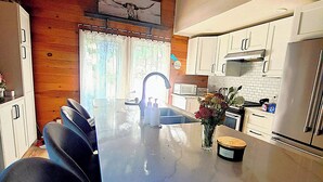 Une cuisine moderne avec des meubles blancs, un plan de travail en marbre, un évier et un coin repas avec des chaises noires.