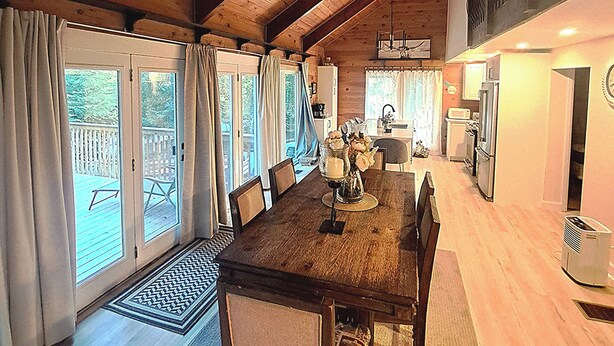 Un vaste espace dédié à la salle à manger, avec une table et des chaises en bois, un lustre et une vue sur la terrasse grâce à de grandes fenêtres.