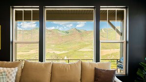 A room with a large window, a sofa, and a piano. - Powder and Lake Days Await | Luxury and Comfort w/ Views & Private Hot Tub (Heber City)
