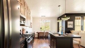 A modern kitchen with wooden cabinets, a central island, and a dining area. - Powder and Lake Days Await | Luxury and Comfort w/ Views & Private Hot Tub (Heber City)