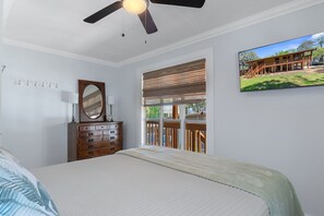 Een slaapkamer met een bed, een dressoir, een plafondventilator, een raam met zonwering en een aan de muur bevestigd schilderij.