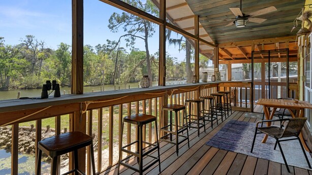 A wooden deck with bar stools and a table, overlooking a body of water and trees. - Peaceful Waterfront Escape on Withlacoochee • Private Dock, Old Florida Charm (Yankeetown)