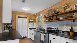 A modern kitchen with wooden accents, white cabinets, a stainless steel oven, and a black countertop. - Peaceful Waterfront Escape on Withlacoochee • Private Dock, Old Florida Charm (Yankeetown)