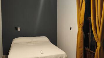 A bedroom with a bed, a ceiling fan, an air conditioner, and yellow curtains.