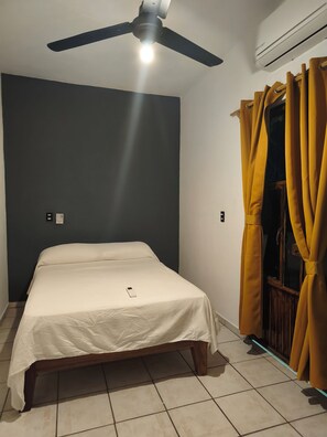 A bedroom with a bed, a ceiling fan, an air conditioner, and yellow curtains.