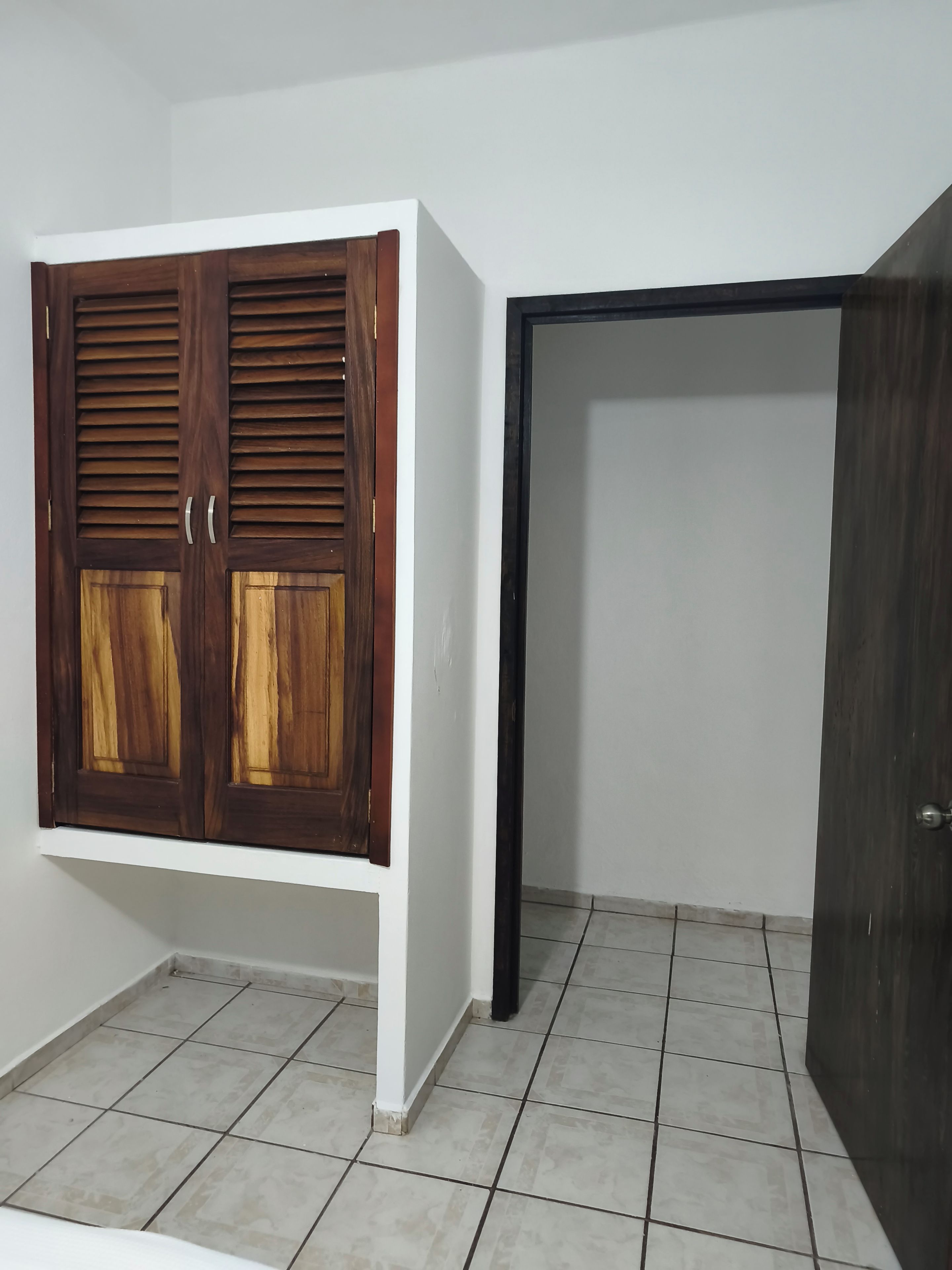 A room with a wardrobe, a door, and tiled flooring.