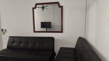 A room with two black leather sofas, a ceiling fan, and a wall-mounted TV.