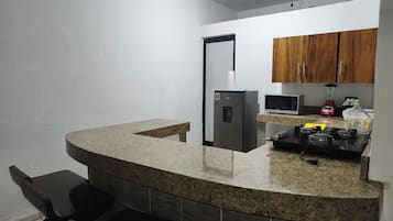 A kitchen with a granite countertop, a refrigerator, a microwave, and wooden cabinets.