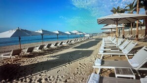 A beach with rows of sun loungers and umbrellas, a clear blue sky, and palm trees. -  Available Oct.22-28th Luxury at its finest!!! 1-Bedroom, 1300 sq ft Condo, (Cabo San Lucas)
