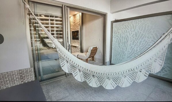 Un hamac sur un balcon, avec une chaise et un mur de pierre en arrière-plan.
