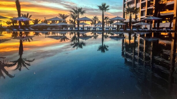 A resort pool with palm trees and umbrellas, surrounded by a multi-story building. -  Available Oct.22-28th Luxury at its finest!!! 1-Bedroom, 1300 sq ft Condo, (Cabo San Lucas)
