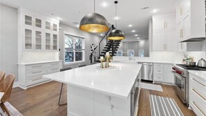 A modern kitchen with white cabinetry, a large island, stainless steel appliances, and pendant lighting. - Uptown Brownstone - 1 Block off Downtown Square (Bentonville)