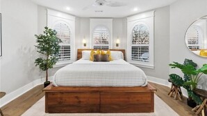 A bedroom with a large bed, a ceiling fan, and two windows with arched tops. - Uptown Brownstone - 1 Block off Downtown Square (Bentonville)