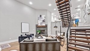 A modern living room with a grey sofa, a fireplace, and a staircase with wooden railings. - Uptown Brownstone - 1 Block off Downtown Square (Bentonville)