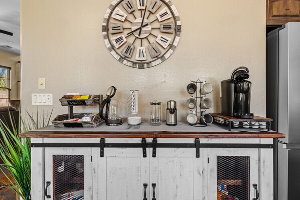 A kitchen counter with a rustic wooden cabinet, a wall clock, and various kitchen appliances. - Mafia Heights! Stunning Backyard, 4 Beds, 3 Baths, Hot Tub/Deep & Large Pool (Goodyear)