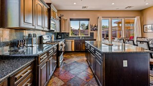 A modern kitchen with dark wood cabinets, granite countertops, and a large island. - Mafia Heights! Stunning Backyard, 4 Beds, 3 Baths, Hot Tub/Deep & Large Pool (Goodyear)