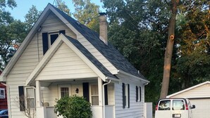 Ein eingeschossiges Haus mit Veranda, Schornstein und Auffahrt, die zu einer Garage führt.