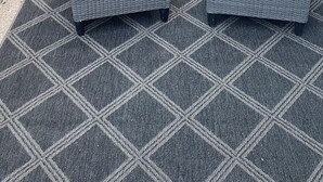 Ein Patio mit zwei grauen Korbstühlen und einem kleinen runden Tisch.