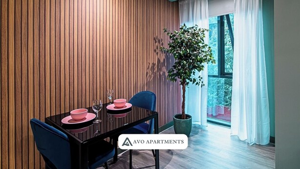 Een moderne eetruimte met een wand van houten panelen, een gedekte eettafel met roze borden en glazen, blauwe stoelen en een potplant.