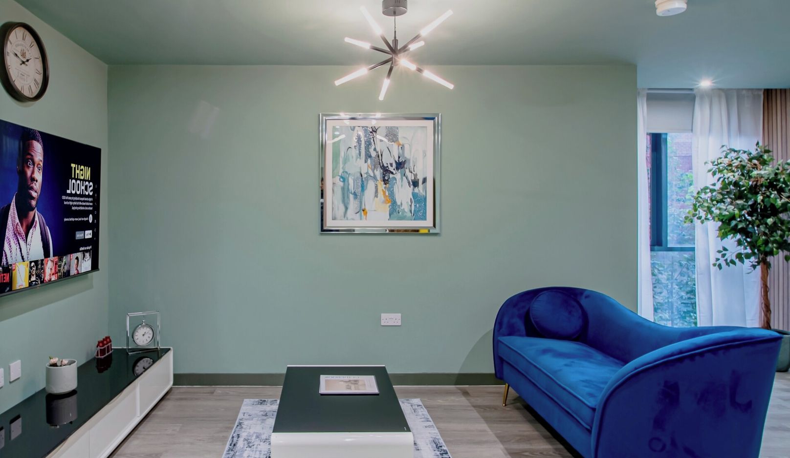 Ein modernes Wohnzimmer mit einem blauen Sofa, einem Couchtisch, einem an der Wand montierten Fernseher und einer Deckenleuchte.