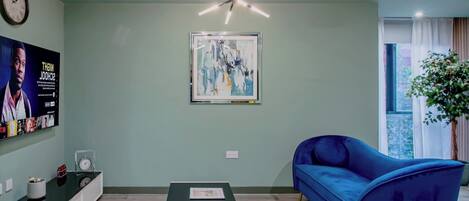 Ein modernes Wohnzimmer mit einem blauen Sofa, einem Couchtisch, einem an der Wand montierten Fernseher und einer Deckenleuchte.