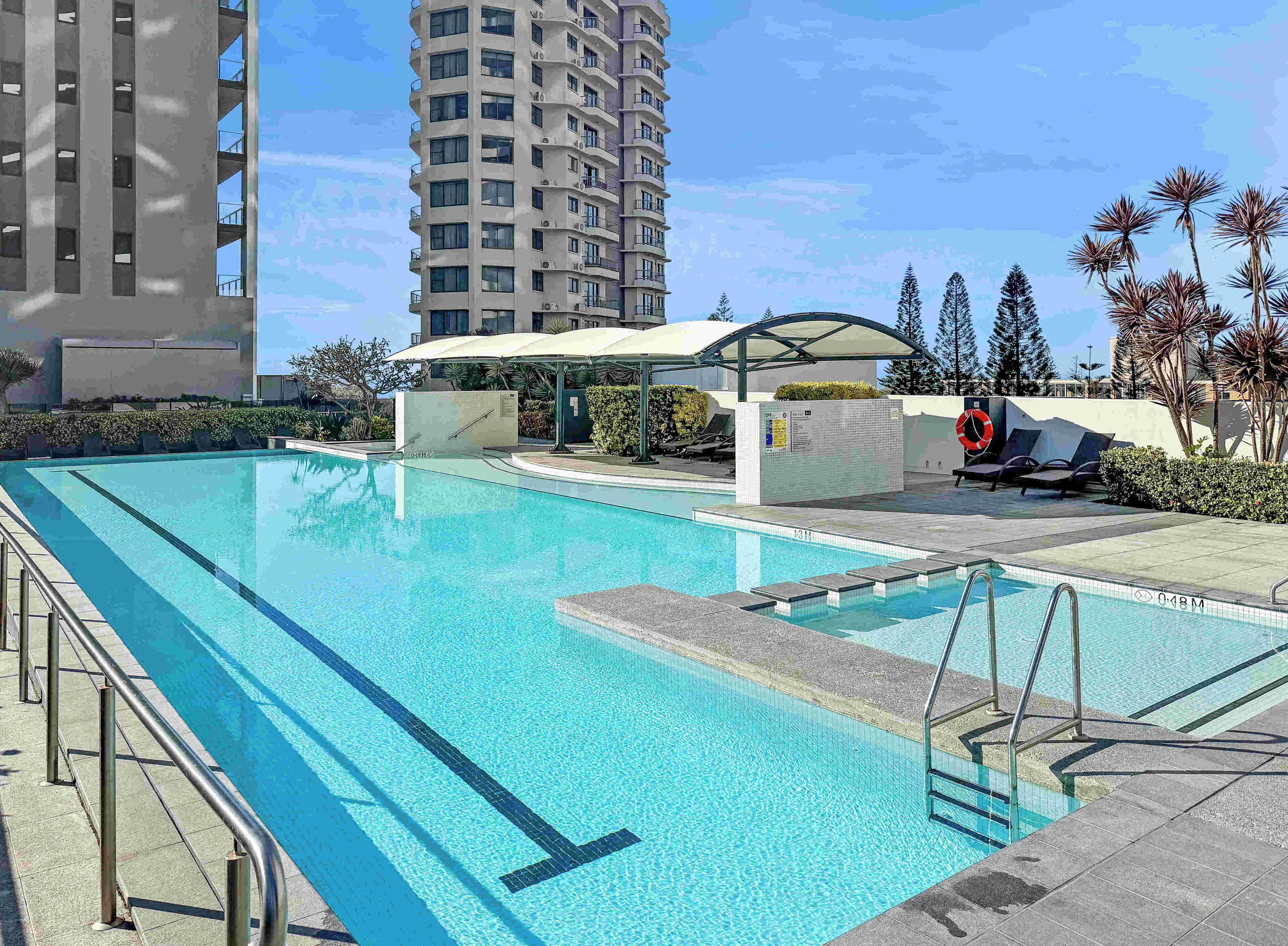 A swimming pool with a sunshade, lounge chairs, and a lifeguard stand.