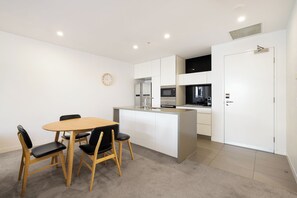 A modern kitchen with white cabinetry, a central island, and a dining area with a wooden table and chairs.